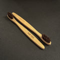 Two bamboo toothbrushes with dark brown horse bristles, one engraved with 'BARE FOLK' and the other with 'BARE FOLK', displayed diagonally on a dark textured background.